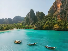 Traditional long-tail boats floating on turquoise waters with limestone cliffs in Thailand.