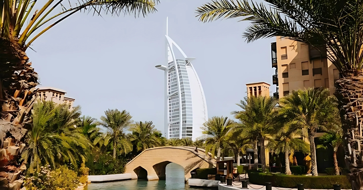 Burj Al Arab hotel in Dubai with palm trees and a stone bridge in the foreground.