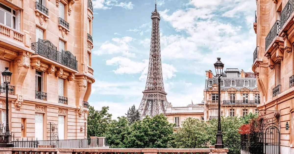Eiffel Tower view framed between Parisian buildings with clear blue sky.