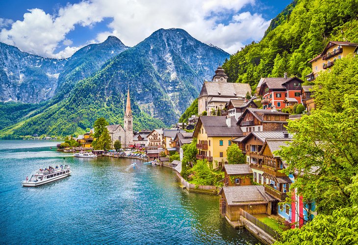 Beautiful lakeside village of Hallstatt in Austria with colorful houses, church spire, boat on the water, and mountains in the background.